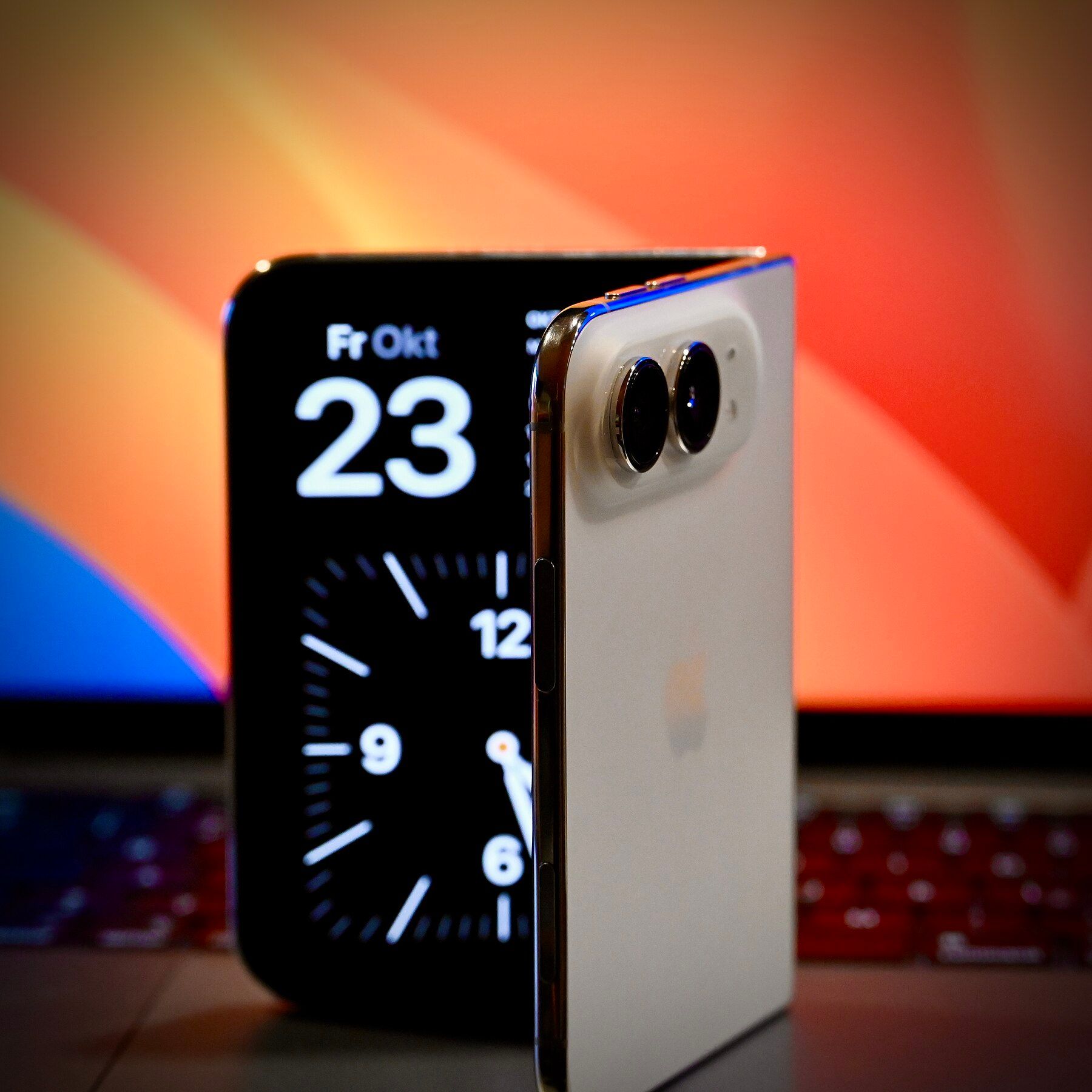 An iPhone Duo standing half open in front of a laptop, showing the date Friday 23 October on its screen