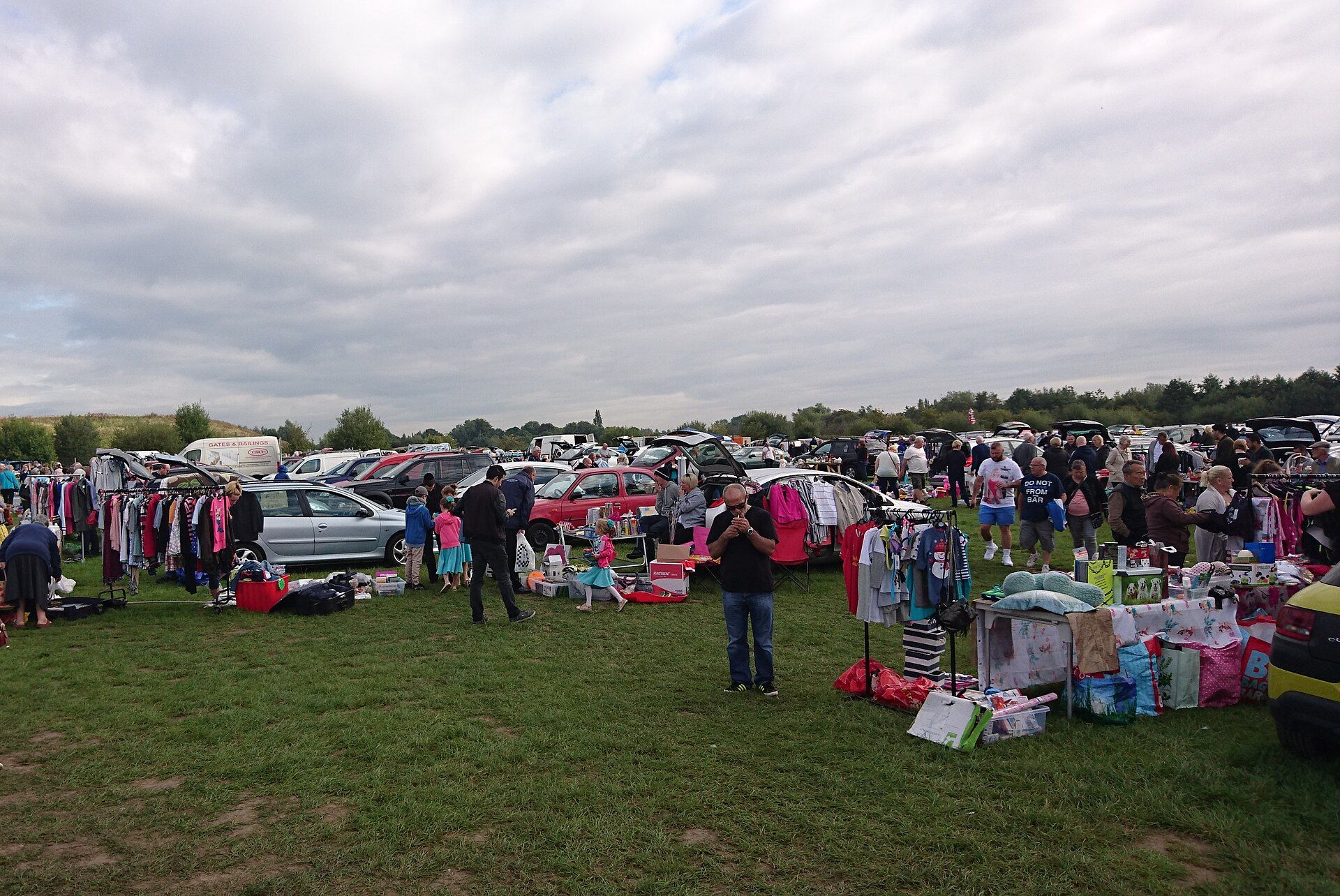 Rows of stalls, clothes rails and car boots at a busy outdoor car boot sale