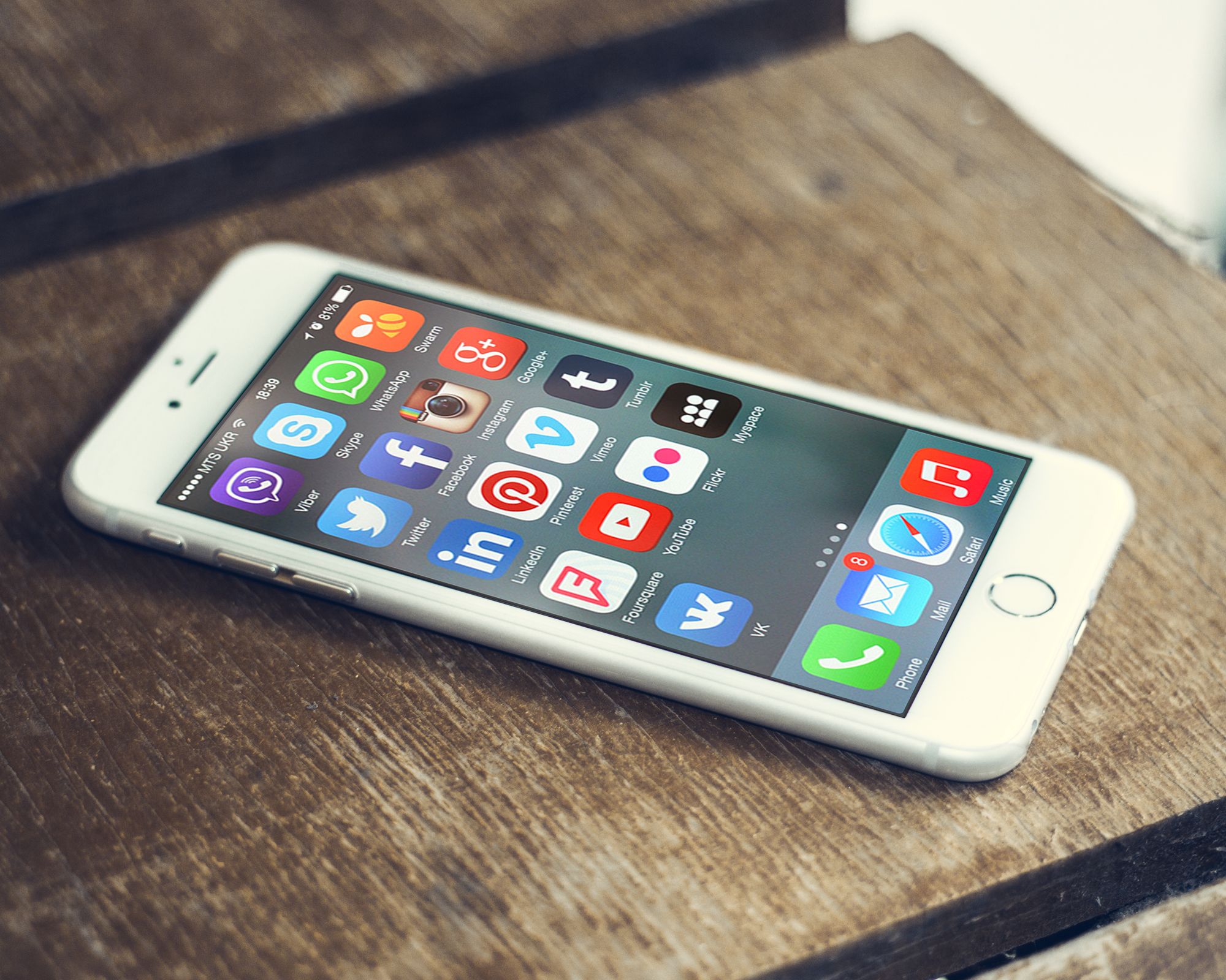A smartphone lying on a wooden table, its screen full of social media app icons